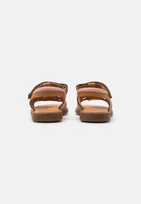 Sandalias de cuero marrón con dos correas ajustables, parte trasera abierta y suela texturizada; plantilla de color marrón claro con un sutil logotipo.