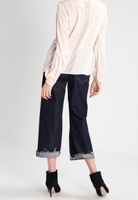 Blusa di seta rosa chiaro con spacco posteriore, abbinata a jeans cropped blu scuro con polsini arrotolati e orli sfilacciati, completata da stivali neri con tacco.
