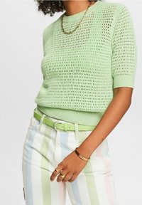 Jasnozielony dzianinowy sweter z krótkim rękawem o teksturowanym wzorze; zestawiony z wielokolorowymi spodniami w paski oraz pasującym zielonym paskiem.