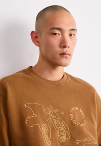 Sudadera marrón con diseño gráfico de líneas amarillas, patrón de texto redondo, cuello de canalé y material de algodón suave.