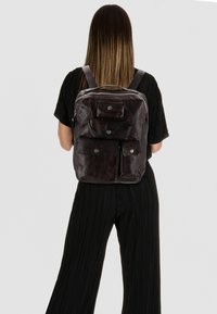 Mochila de cuero marrón oscuro con múltiples bolsillos exteriores, cierre de cremallera, correas ajustables y una textura suave.