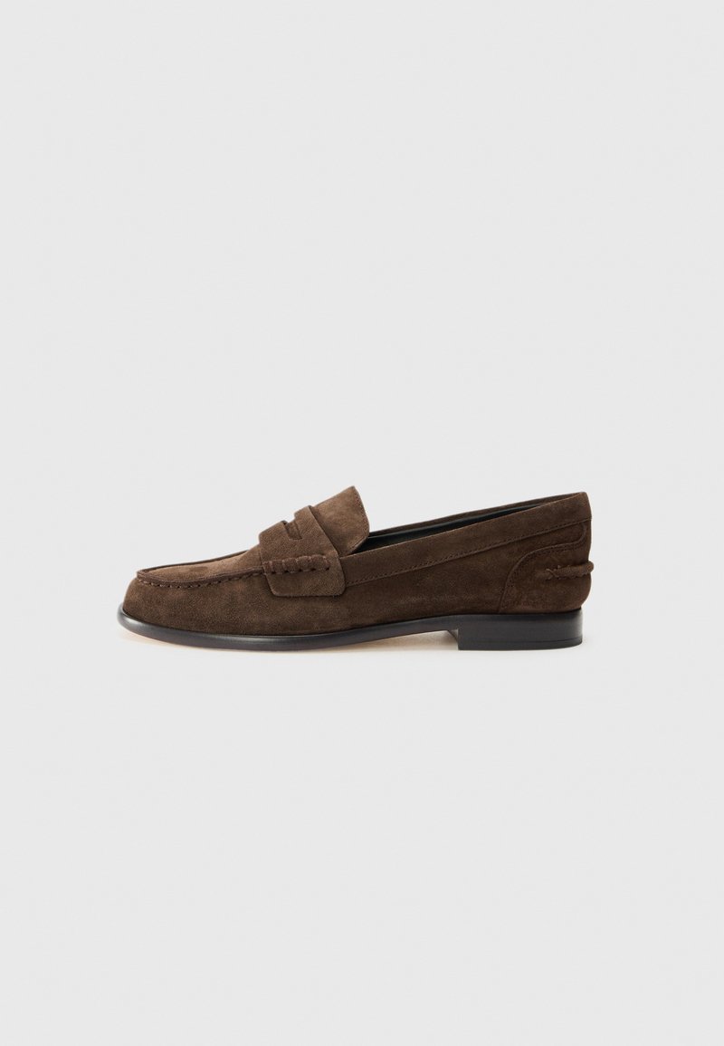 Mocasines de ante marrón con un tacón bajo, que presentan un diseño de delantal cosido y un forro interior suave. Los acentos laterales añaden textura.