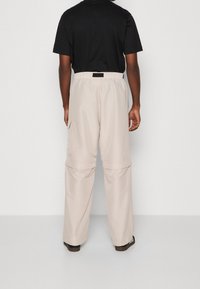 Beige cargo kalhoty s elastickým pasem na šňůrku, dvěma bočními kapsami a volným střihem. Materiál vypadá hladce s matným povrchem.