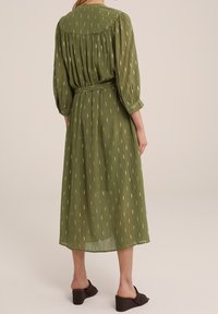 Grön midiklänning med löst sittande passform, 3/4 ärmar, midjeband och vertikala vita mönster. Lättviktsmaterial med struktur och rundad halsringning.