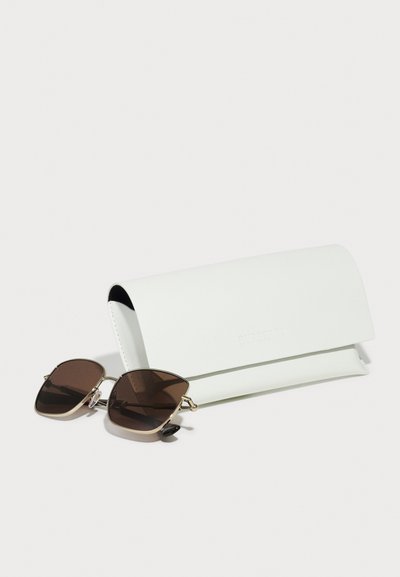 Sonnenbrille mit braunen Gläsern, goldenen Metallakzenten und einer einzigartigen Form, neben einem weißen Lederetui mit dem eingeprägten Schriftzug "Burberry".