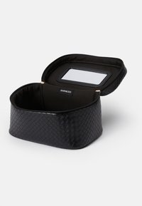 Etui cosmetic din material țesut negru, cu un vârf curbat, închidere cu fermoar și oglindă interioară. Captuseală din material moale și etichetă de marcă în interior.