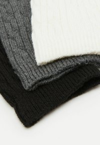 Trzy dziane czapki o prążkowanej strukturze w różnych odcieniach: kremowym, ciemnoszarym i czarnym. Tekstura jest miękka i puszysta, podkreślająca ciepło i komfort.