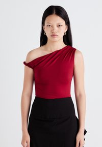 Top rosso a spalla singola in tessuto liscio con dettaglio di scollatura drappeggiata, abbinato a una gonna nera. Il design presenta una silhouette aderente.