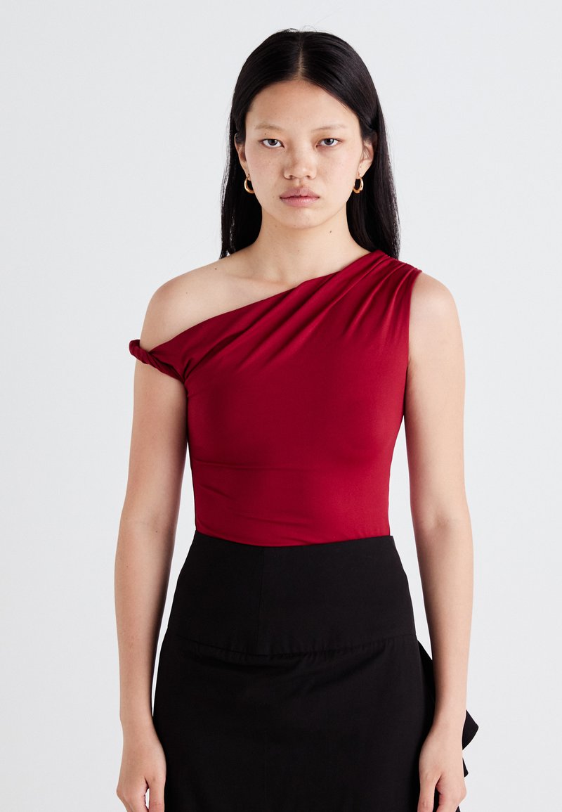 Top rosso a spalla singola in tessuto liscio con dettaglio di scollatura drappeggiata, abbinato a una gonna nera. Il design presenta una silhouette aderente.