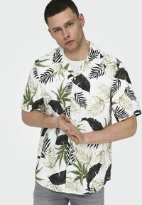 Camisa de manga corta con botones, base blanca con patrones de hojas negras y verdes, corte relajado, tela ligera, cuello y textura sutil.