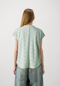 Top de manga corta verde claro con un diseño texturizado de ojetes y un dobladillo curvado, combinado con pantalones cortos de denim holgados.