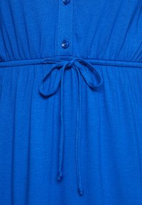 Abito blu realizzato in tessuto testurizzato, caratterizzato da una chiusura con bottoni frontale, vita elastica e una cintura per la regolazione. Finitura liscia con dettagli arricciati.