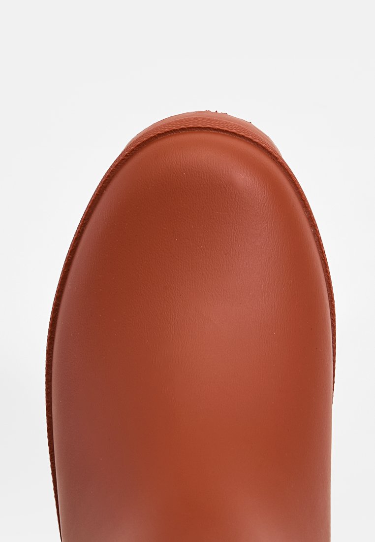 Zapato de goma marrón con punta redondeada, textura mate suave y bordes elevados. El diseño es simple, sin patrones ni acentos adicionales.