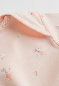 Šviesiai rožinė medžiaga su pasikartojančiu mažų fėjų, gėlių ir širdelių raštu. Minkšta tekstūra su šonkauline apykaklės detaile.