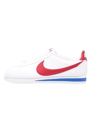 Biały but sportowy Nike z czerwonym logo typu swoosh, czerwoną zakładką na pięcie i niebieskim paskiem na białej podeszwie, widok z boku, bez tła.