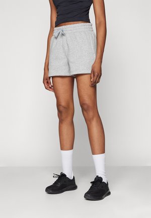 Pantalones cortos de algodón gris con cintura elástica y cordón, con bolsillos laterales. Combinados con una camiseta negra, calcetines blancos y zapatos negros.