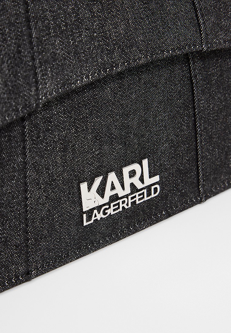 Sac en denim noir avec une surface texturée, présentant des coutures surpiquées et un logo argenté affichant "KARL LAGERFELD" de manière bien visible.