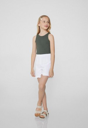 Débardeur vert côtelé, shorts blancs à taille élastique et sandales beige clair avec semelles épaisses. Design simple, sans motifs ni graphismes.