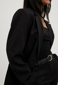 Must mustreev mustaga laia krae ja pehme tekstiiliga, kantud musta topi peal. Kootud must vöö hõbedase pandlaga rõhutab vöökohta.