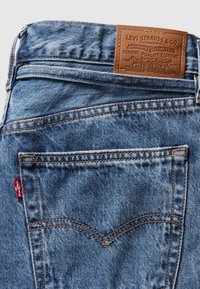 Lichtblauwe denim jeans met een bruine leren patch met reliëftekst, contraststeken en een rood Levi's label op de achterzak.