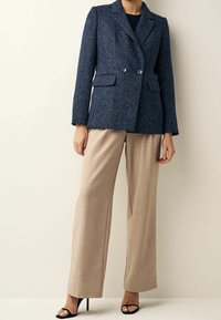 Blazer azul marino texturizado con dos botones y solapas con muesca, combinado con pantalones de pierna ancha color beige claro y sandalias negras de tacón alto.