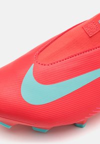 Sarkans sintētiskais futbols apavi ar teksturētu virsmu, aprīkoti ar izteiktu gaiši zilo Nike swoosh sānos un aerodinamisku dizainu.