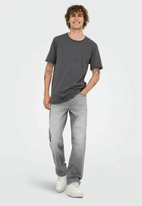 Sivé tričko s okrúhlym výstrihom v kombinácii so svetlosivými džínsami. Džínsami sú rovného strihu so zrolovanými spodnými časťami, doplnené bielymi teniskami.