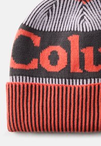 Căciulă tricotată în negru, gri și portocalie vibrantă, având litere îndrăznețe și un tiv cu dungi ribbed, cu un design texturat și patterned.