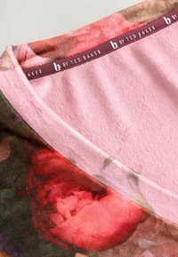 Bluzka w kwiatowy wzór z różowym, miękkim wykończeniem przy szyi i żywymi wzorami róż, z markowym oznaczeniem "b by Ted Baker" na wewnętrznej metce.