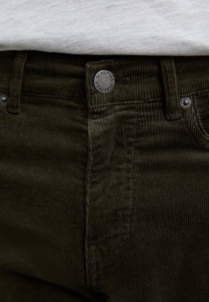 Pantalones de pana verde oscuro con una tela texturada, botones de metal y una marca en la cinturilla. Costuras visibles y bolsillos.