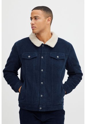 Chaqueta de pana azul marino con cuello de piel sintética crema, cierre frontal de botones, dos bolsillos en el pecho y bolsillos laterales para las manos. Detalle de tejido texturizado.