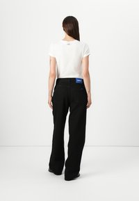 Black wide-leg jeans with a blue label at the waist and embroidered details, paired with a fitted white T-shirt. The background is plain white.