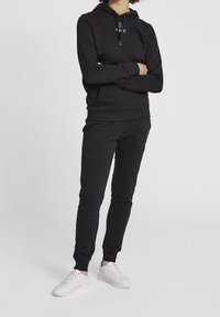 Svart bomullshuvtröja med dragsko och logotyp, i kombination med matchande smal ben joggers. Vita sneakers fulländar outfiten.