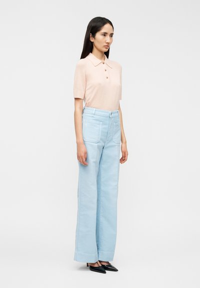 Ροζ  ανοιχτό ροζ πόλο μπλουζάκι με κοντά μανίκια και τρία κουμπιά, σετ με ψηλόμεσο ανοιχτό μπλε παντελόνι με φαρδιά μπατζάκια και μαύρα μυτερά παπούτσια.