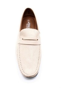 Mocassin en daim beige avec bout fermé, une sangle décorative et des détails de couture. La doublure intérieure est marron, avec une texture lisse tout au long.