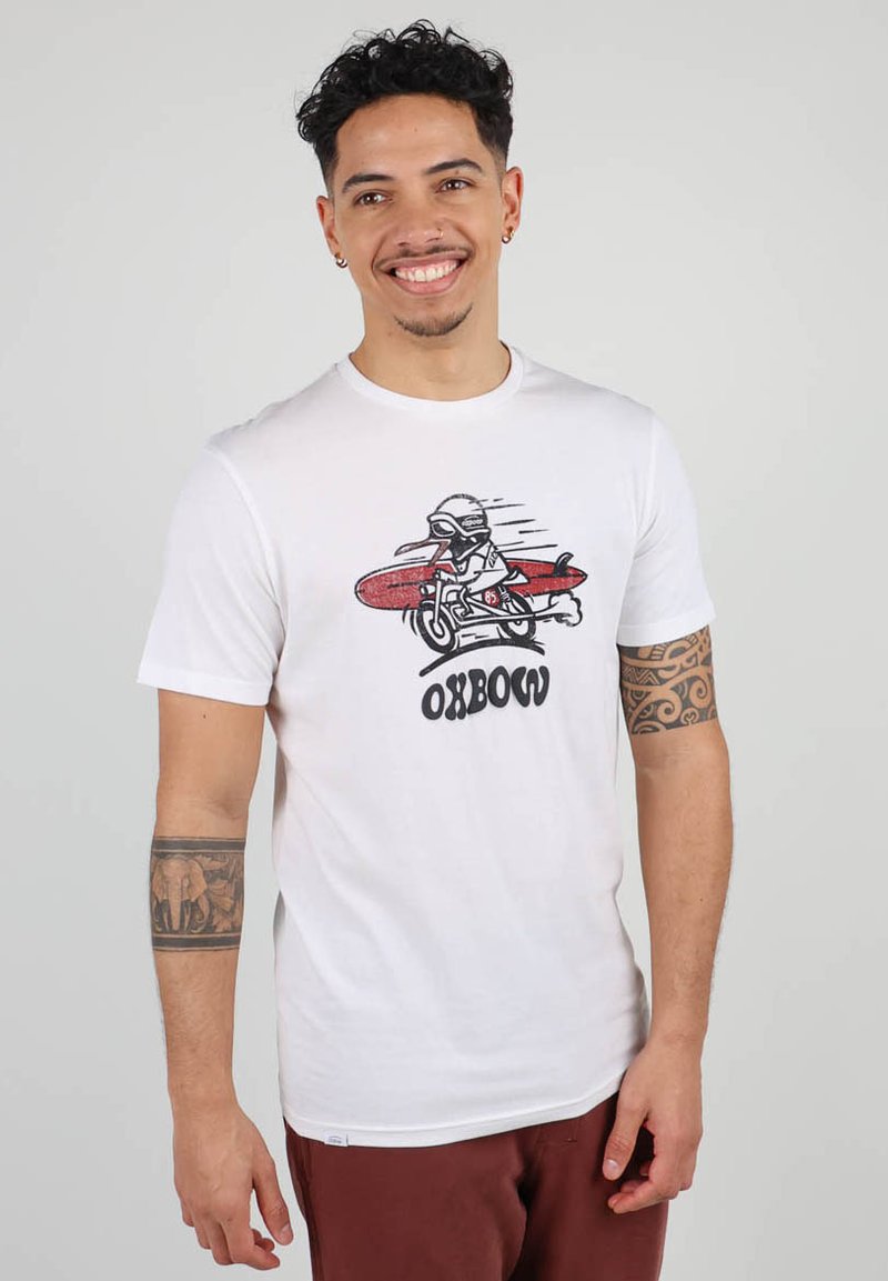 T-shirt blanc en coton avec un graphique représentant un motard sur une planche de surf rouge. Le texte en dessous dit "OXBOW". Manches courtes avec un col rond.