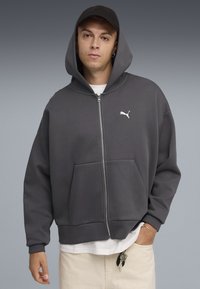 Grijze zip-up hoodie van zacht materiaal met een relaxte pasvorm. Kenmerken zijn een kangoeroezak, capuchon en een wit Puma-logo op de borst.