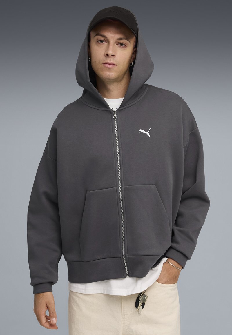 Grijze zip-up hoodie van zacht materiaal met een relaxte pasvorm. Kenmerken zijn een kangoeroezak, capuchon en een wit Puma-logo op de borst.