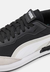 Černé a šedé tenisky s nubukovým a textilním svrškem, bílým logem PUMA, černými tkaničkami a bílou mezipodešví. Zaoblená špička a texturované akcenty.