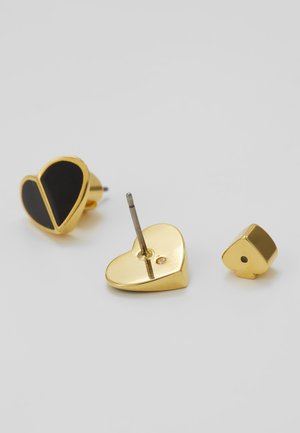Boucles d'oreilles clous en forme de cœur en or, dont une avec un motif en émail noir, présentées de face, de dos et avec des parties de fermoir séparées sur une surface blanche.