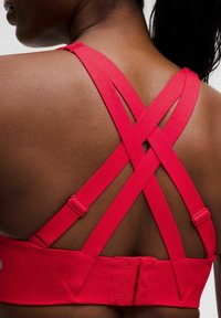 Sostén deportivo rojo con tirantes entrecruzados en la parte posterior y cierres ajustables; textura suave y diseño elegante. Ajuste de gancho y ojo en la parte posterior.
