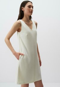 Abito bianco senza maniche con scollatura a V, dotato di una tasca frontale e di una vestibilità rilassata, realizzato in tessuto morbido con una leggera lucentezza.