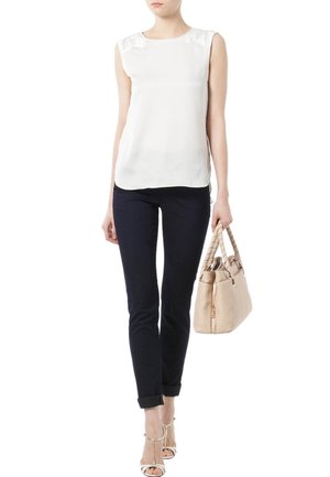 Bílá halenka bez rukávů s krajkovým detailem na rameni, doplněná tmavými úzkými džíny a béžovou taškou, doplněná sandály na podpatku s pásky.