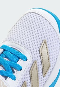 Valge sportlik jalanõu hingava võrgust pealismaterjaliga, siniste paelte ja beežide detailidega, tekstuurse pinnaga ja polsterdatud kraega mugavuse tagamiseks.