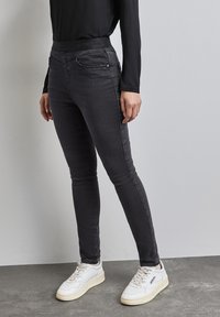 Svarta skinny jeans i denim med hög midja, framfickor och subtila sömnadsdetaljer, som är kombinerade med vita sneakers på en grå yta.