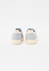 Light blue suede sneakers with beige accents, featuring a rounded silhouette and a textured sole. Branding on the heel.