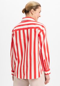 Red and white striped shirt with long sleeves, a collar, and buttoned cuffs. Made from lightweight fabric, featuring visible seams and pleats.