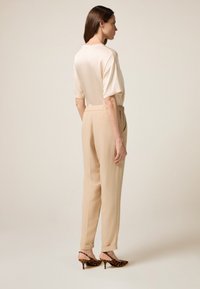 Pantalons plissés beige à coupe décontractée, associés à un chemisier crème doux. Accentués par des escarpins à imprimé léopard pointus.
