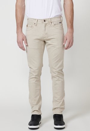 Jeans beige de corte slim, elaborados con una mezcla de algodón, que presentan una cremallera con cierre de botón, cinco bolsillos y detalles de costura sutiles.