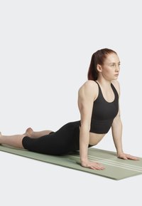 Svart kortärmad tränings topp och leggings på en person i en yogaposition på en ljusgrön matta med randigt mönster.